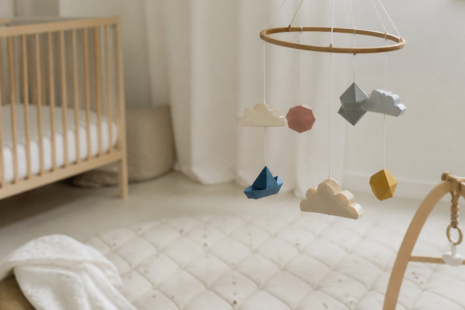 Mobile en formes de papier suspendu à un cercle de bois au-dessus d’un tapis de jeu clair