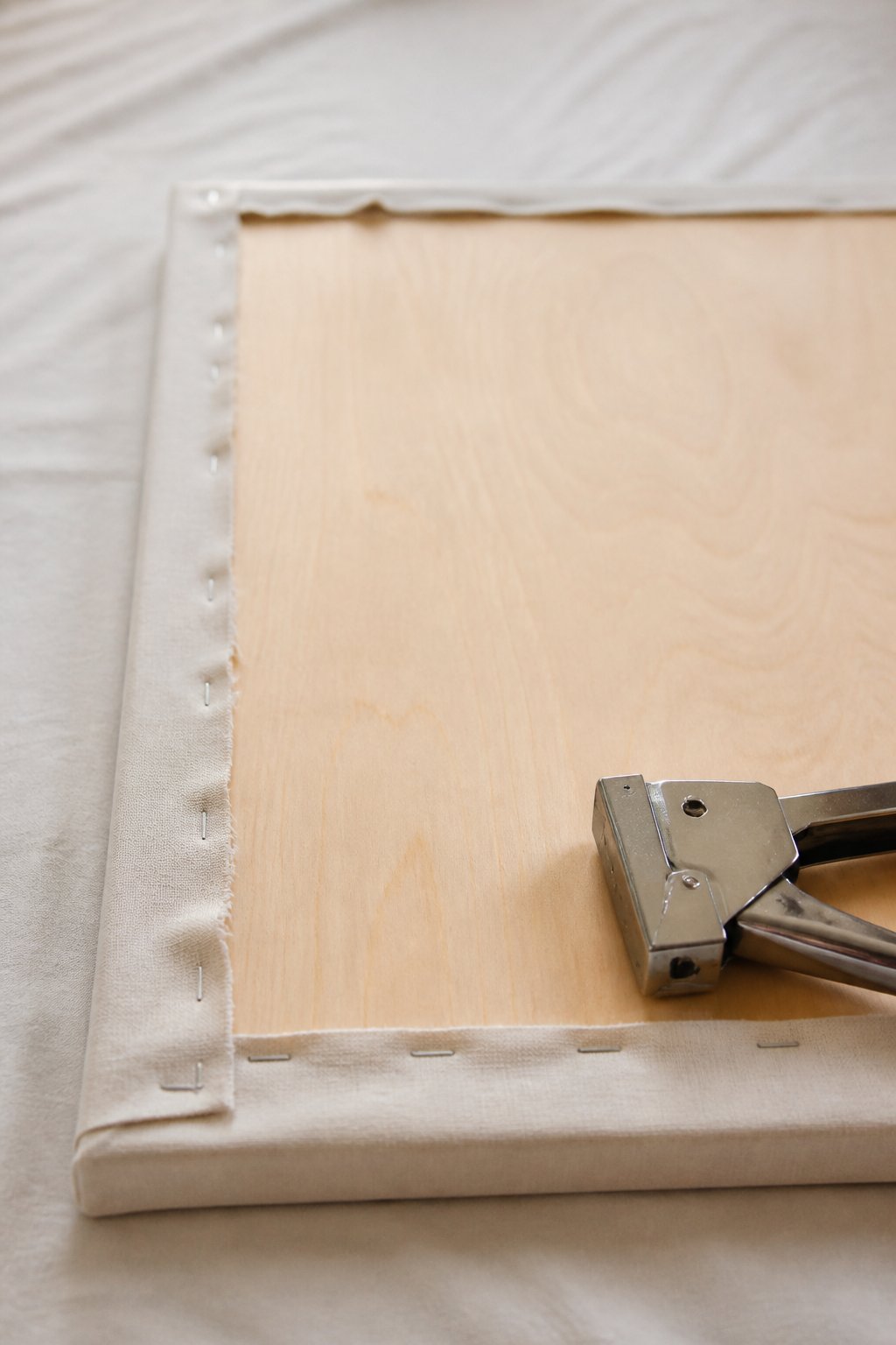 Dos d’un panneau de tête de lit avec le tissu rabattu et agrafé sur le contreplaqué, agrafeuse posée à côté
